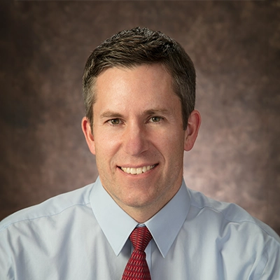 Eye Doctor Andy Rockwood Smiling In Front Of Brown Background
