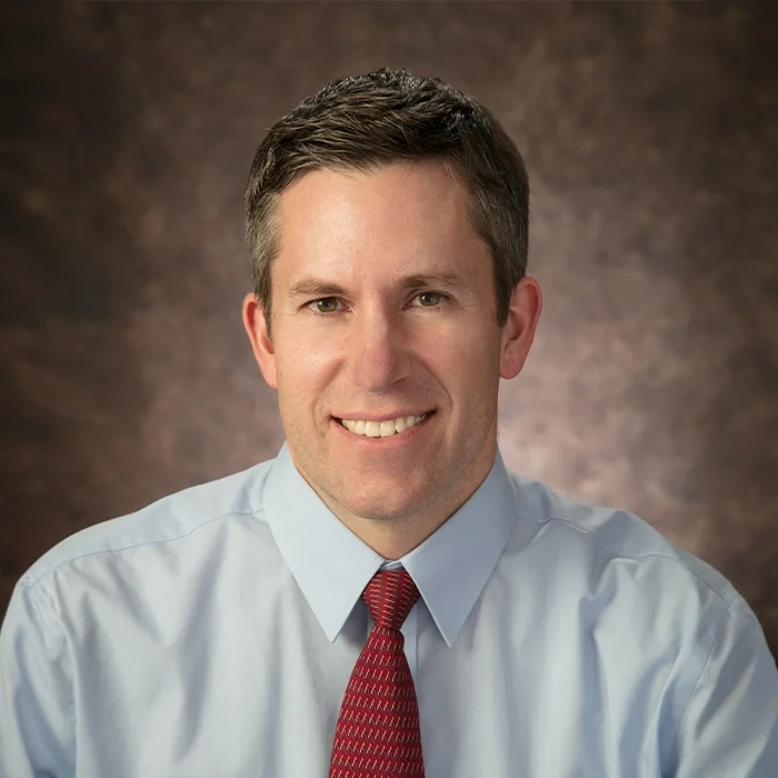 Eye Doctor Andy Rockwood Smiling In Front Of Blurred Brown Background